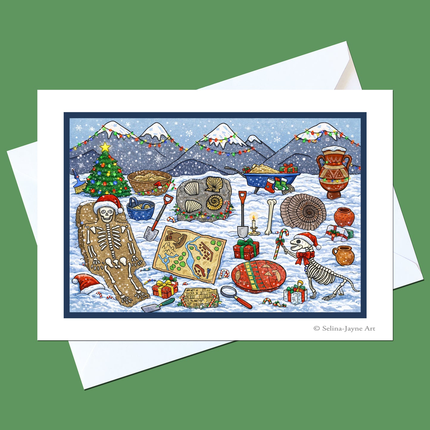 A square art print or greeting card featuring a whimsical winter holiday scene with skeletons, snow, mountains, gifts, and holiday decorations, shown on top of white envelopes against a solid green background.