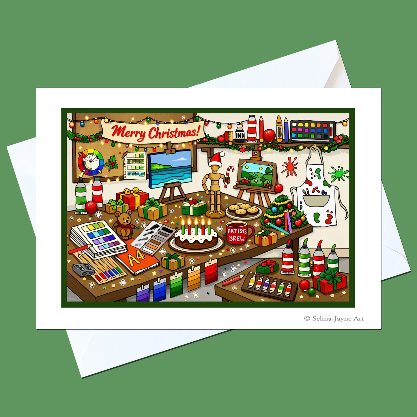 A Christmas-themed art print card featuring a detailed illustration of a colorful art studio decorated for the holiday, shown with white envelopes on a solid green background.