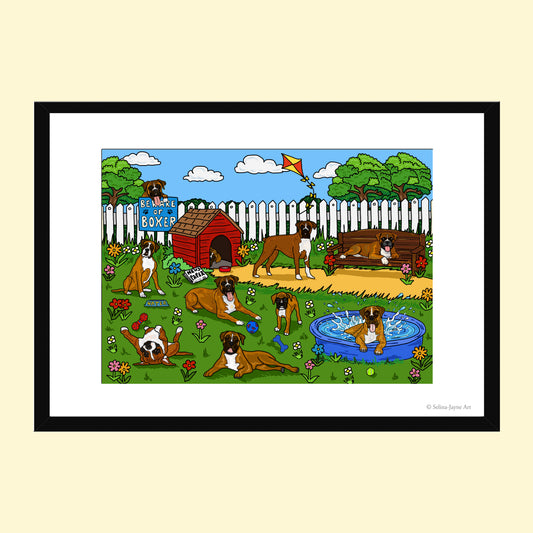 A framed art print featuring a colorful cartoon illustration of several Boxer dogs in a backyard scene with a doghouse, fence, trees, pool, and kite. The print is presented with a white mat and a black frame against a light beige background.
