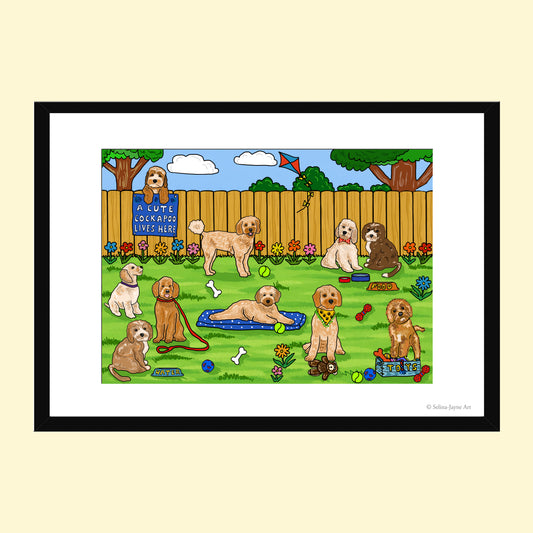 A framed art print featuring a colorful cartoon illustration of multiple dogs playing in a backyard with a wooden fence, trees, flowers, and toys. The print is presented with a white mat and a black frame against a pale cream background.