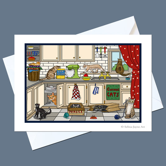 A printed art card or greeting card featuring a whimsical illustrated kitchen scene with multiple cats, shown with white envelopes on a muted blue-gray background. The artwork includes cream cabinets, a green mixer, a red curtain, and several cats in different poses.
