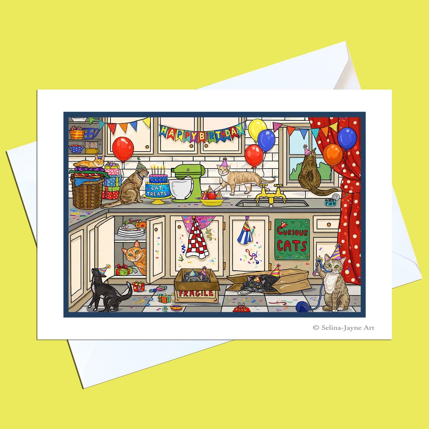 A printed art card featuring a whimsical illustrated kitchen scene with multiple cats, balloons, banners, and holiday decorations, shown with white envelopes on a pale yellow background. Small text at the bottom right reads '© Selina Jayne Art'.