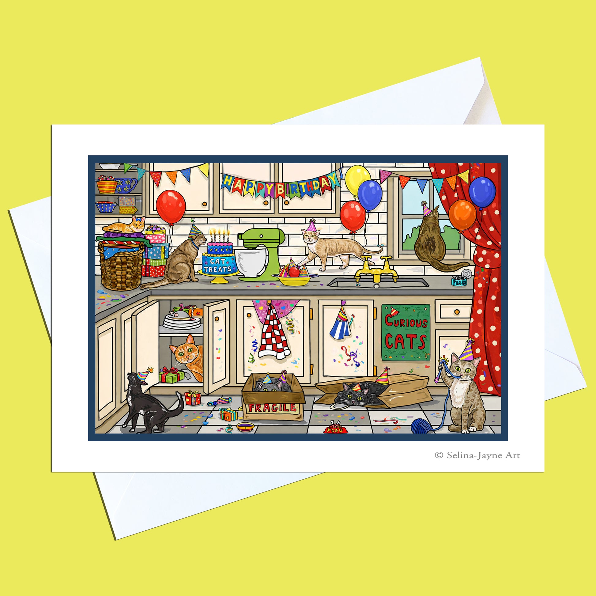 A printed art card featuring a whimsical illustrated kitchen scene with multiple cats, balloons, banners, and holiday decorations, shown with white envelopes on a pale yellow background. Small text at the bottom right reads '© Selina Jayne Art'.