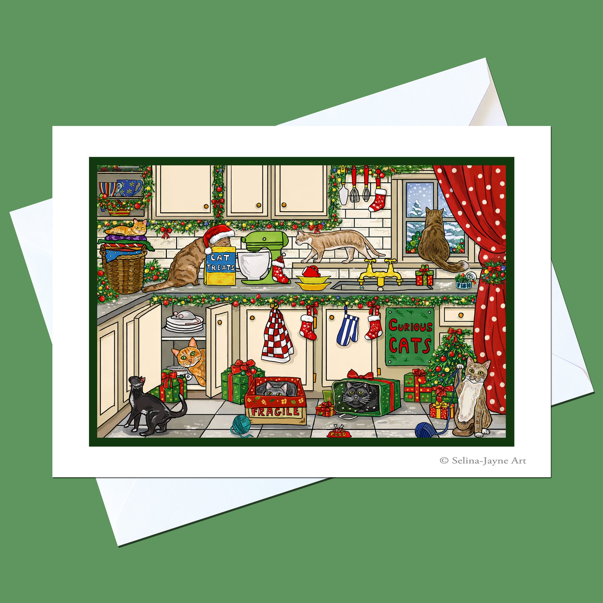 A Christmas-themed kitchen art print featuring cats in a decorated kitchen, shown with a white envelope on a solid green background. The print has a white border and the artist's name 'Selina Jayne Art' is printed in the bottom right corner.
