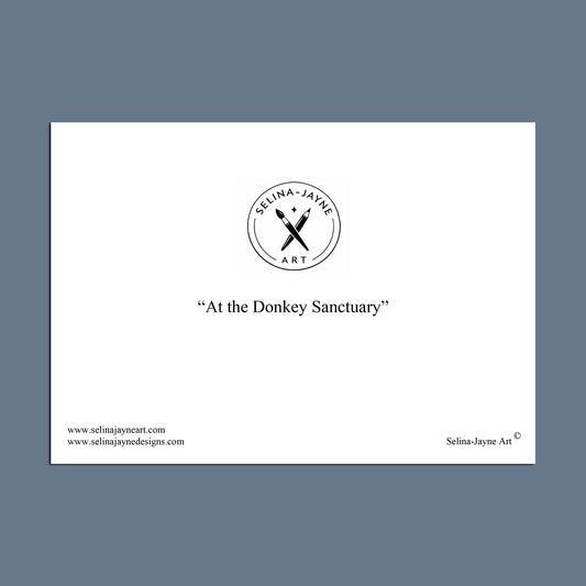 A minimalist art print preview featuring the text 'At the Donkey Sanctuary' centered on a white rectangular card, with the Selina Jayne Art logo above and website text along the bottom, set against a slate blue background.