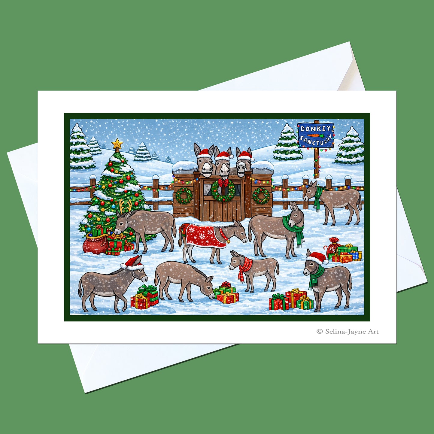 A Christmas-themed art print featuring donkeys in a snowy scene with a decorated tree, gifts, and a sleigh, shown on a white card with an envelope against a solid green background.