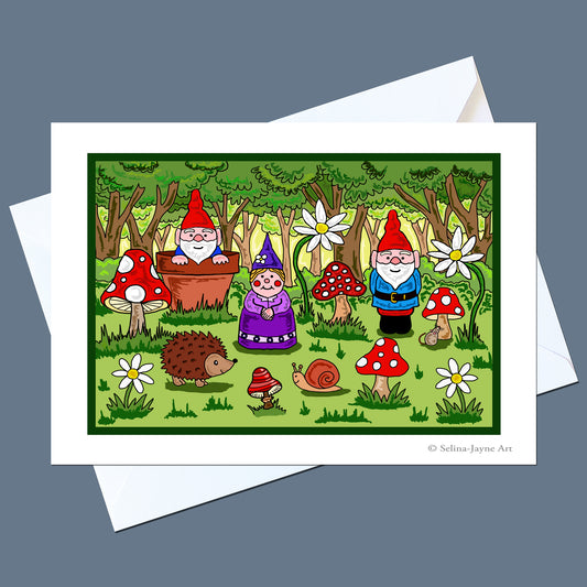 A square art print or card featuring a whimsical forest scene with garden gnomes, mushrooms, flowers, a hedgehog, and a snail, shown with white envelopes behind it on a muted blue-gray background.
