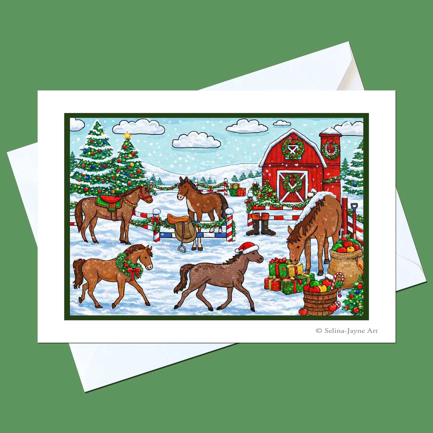 A holiday-themed art print featuring horses around a red barn in a snowy landscape, displayed on a white envelope against a solid green background.