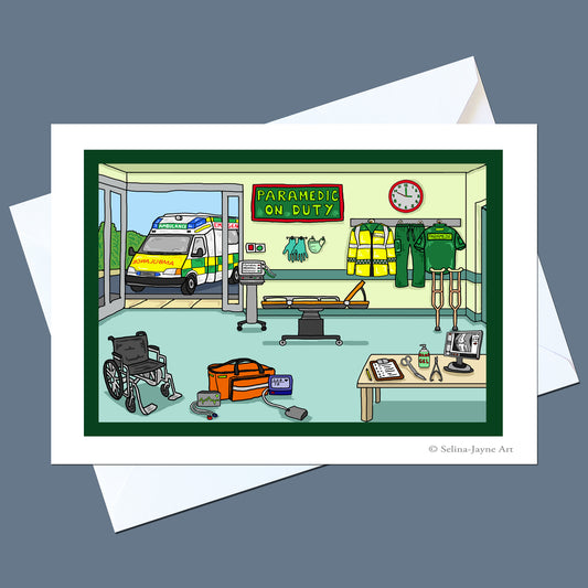 A rectangular art print or card showing a cartoon ambulance station interior with an ambulance, paramedic uniforms, stretcher, wheelchair, and equipment, displayed on top of white envelopes against a muted blue-gray background.