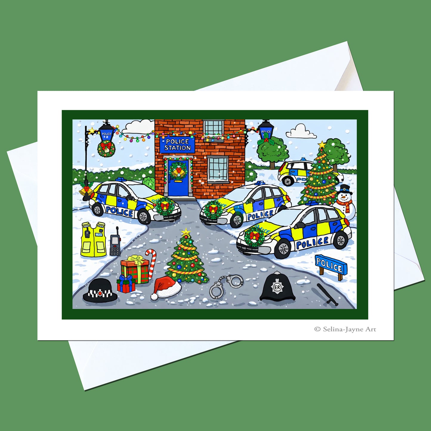 A Christmas-themed police station greeting card with a white envelope behind it, shown on a solid green background. The illustration features decorated police cars, a brick station, snow, gifts, and holiday trees.