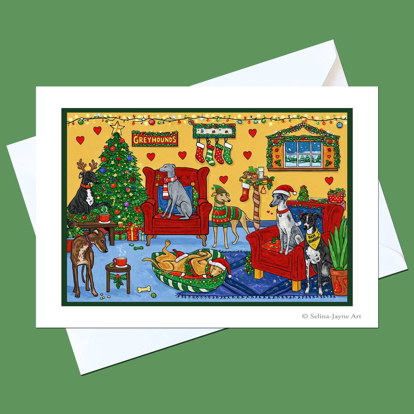 A holiday art print card featuring greyhounds in a cozy Christmas living room with a tree, stockings, and red chairs, shown with a white envelope on a green background.