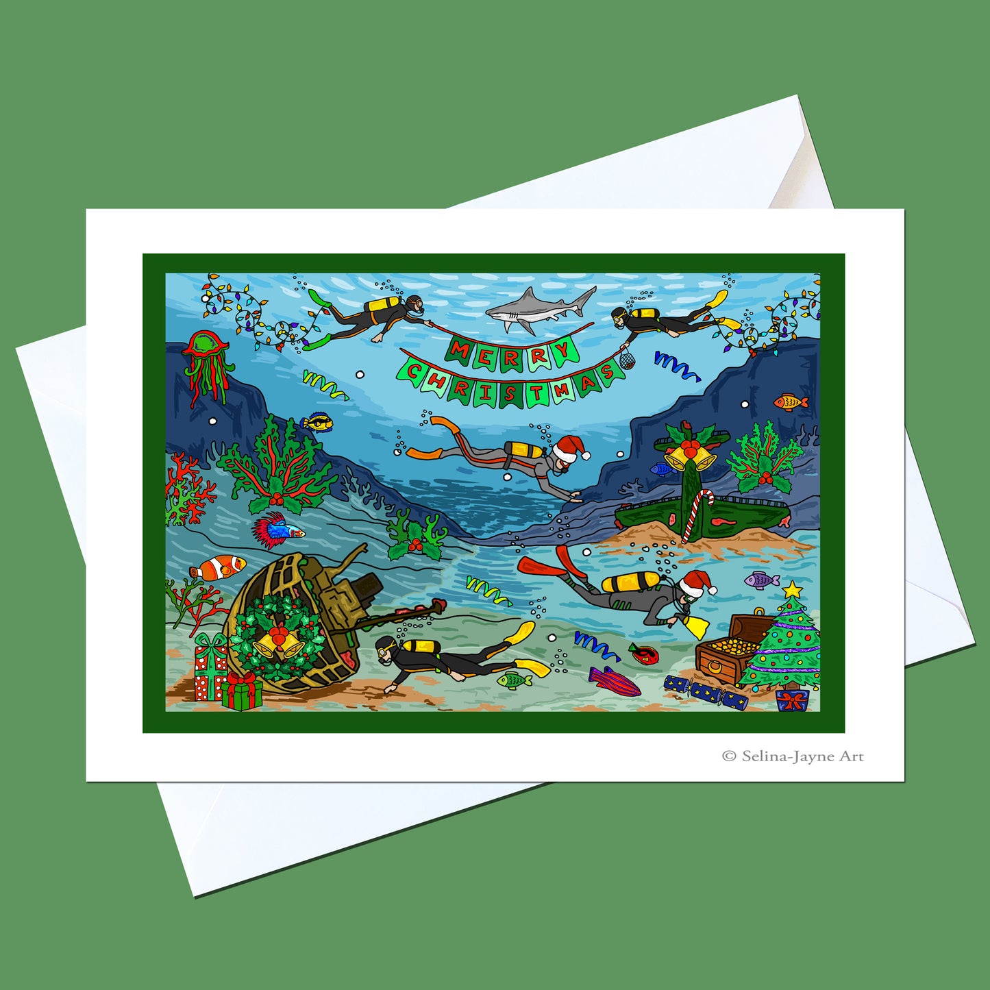A square greeting card with a white border and white envelope, featuring a colorful underwater Christmas scene with divers, a shark, a banner reading 'Merry Christmas', and a shipwreck. The card is shown on a solid green background.