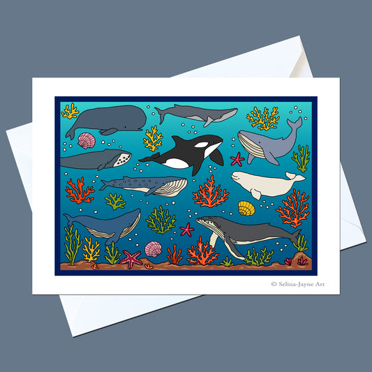 A square art print featuring an underwater scene with whales, dolphins, coral, and starfish on a blue ocean background, shown with a white envelope on a slate gray backdrop. The print includes the text '© Selina Jayne Art' in the lower right corner.